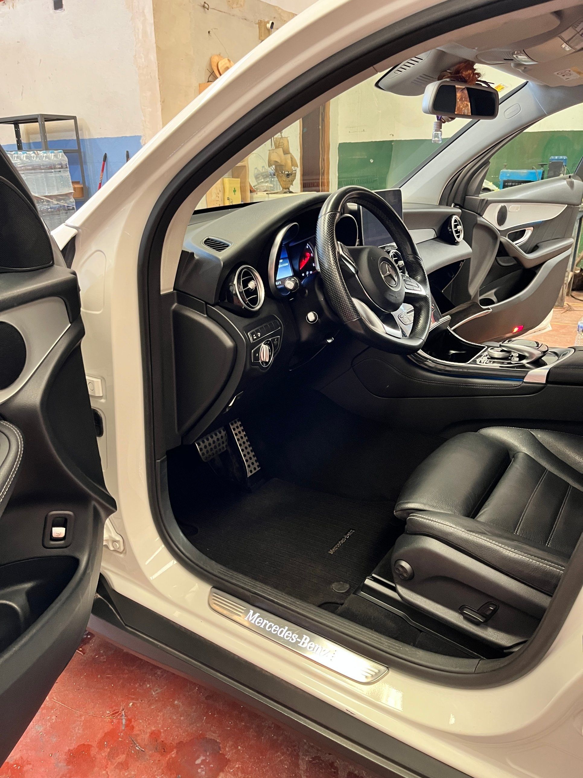 Interior de un Mercedes GLC blanco con la puerta abierta: volante, salpicadero y asiento de piel negra limpios