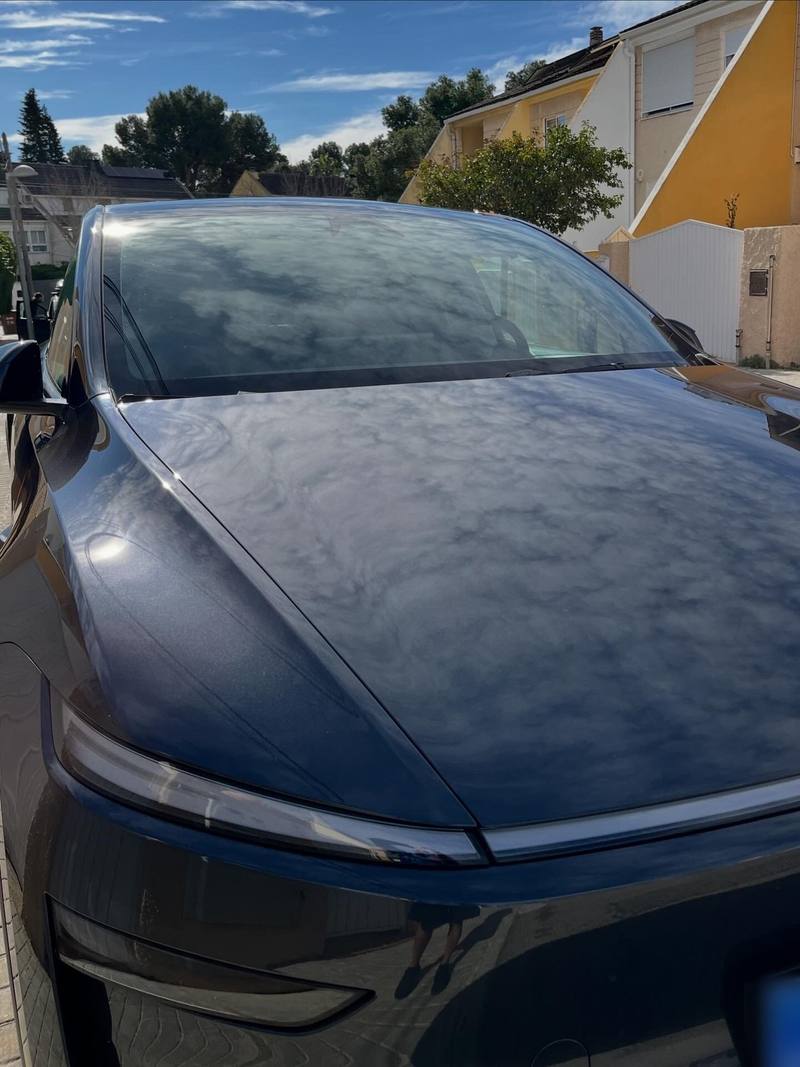 Capó de un Tesla azul oscuro brillante tras el lavado, reflejando el cielo