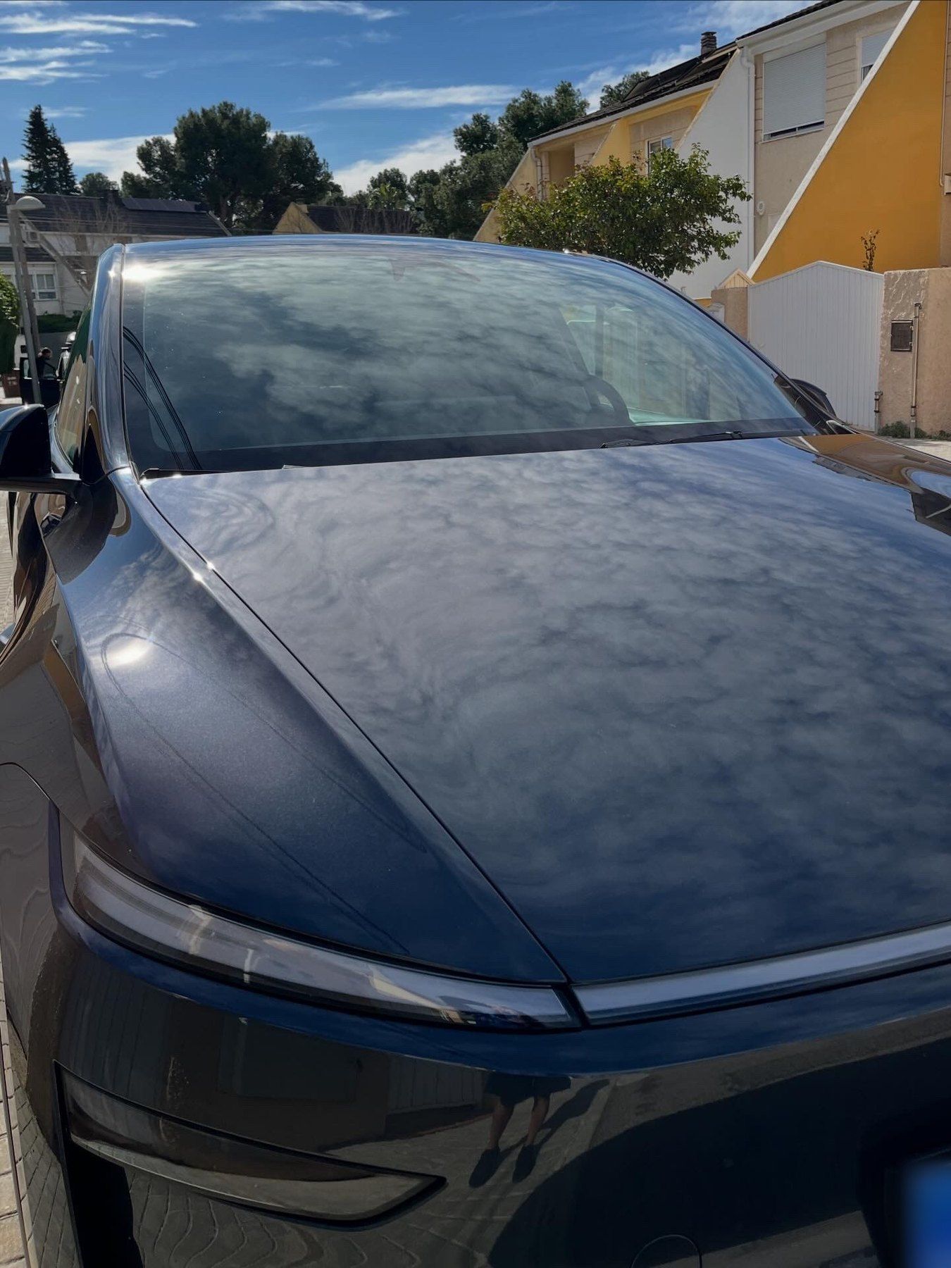 Capó de un Tesla azul oscuro brillante tras el lavado, reflejando el cielo